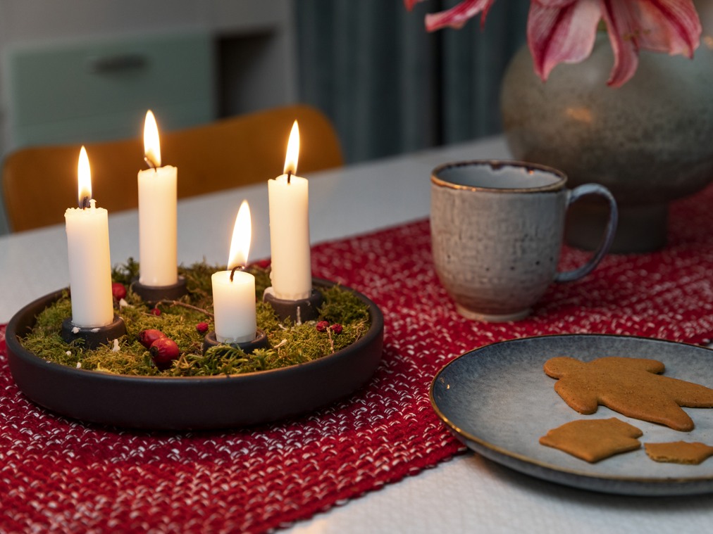 Bord med levande ljus, röd duk, kaffekopp och fat med pepparkakor.