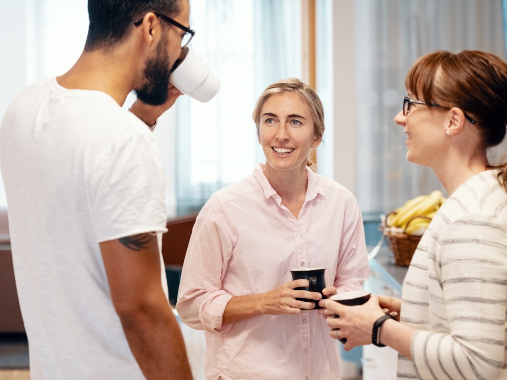 Några personer med kaffemuggar i händerna som pratar med varandra.